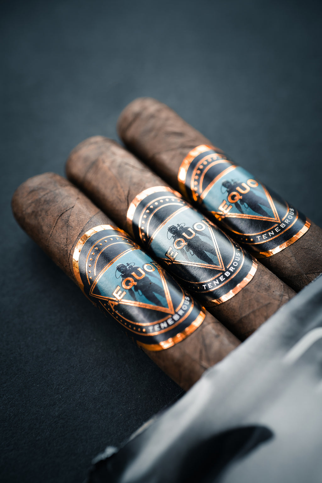 Three Tenebrous Aequor cigars with 'premium' labels on a dark background